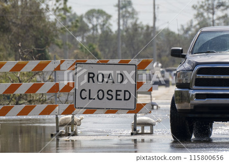 Flooded street in Florida after hurricane rainfall with road closed signs blocking driving of cars. Safety of transportation during natural disaster concept 115800656