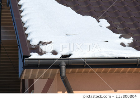 Closeup of house roof top covered with snow in cold winter. Tiled covering of building in wintertime weather Closeup of house roof top covered with snow in cold winter. Tiled covering of building in wintertime weather 115800804