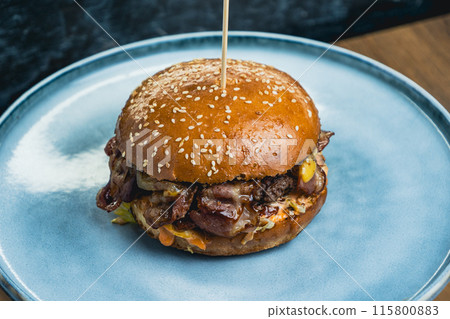Tasty burger served on a large blue plate, placed indoors on a wooden surface Tasty burger served on a large blue plate, placed indoors on a wooden surface 115800883