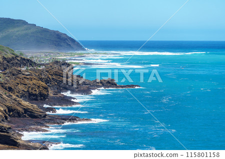 A scenic view of a cliff facing the ocean with waves breaking on the sandy beach 115801158