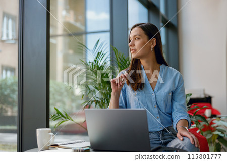 Young professional woman is focused on her laptop work at a bright modern office desk by the window 115801777