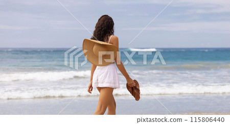 Woman Walking on Beach Holding Sandals and Sun Hat on Shoulder Woman Walking on Beach Holding Sandals and Sun Hat on Shoulder 115806440