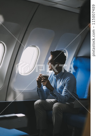 Asian businessman enjoying enjoys a coffee comfortable flight while sitting in the airplane cabin, Passengers near the window. Asian businessman enjoying enjoys a coffee comfortable flight while sitting in the airplane cabin, Passengers near the window. 115807489