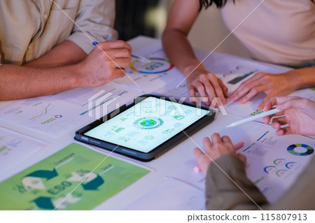 close up diversity team brainstorming focused on ESG (environment,social,governance)  with tablet or sdgs goals in a sustainable green office at night 115807913