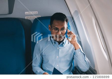Attractive Asian male passenger of airplane sitting in comfortable seat while working laptop and tablet with mock up area using wireless connection. Travel in style, work with grace. 115808899