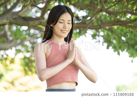 Woman doing yoga in green park (outdoor portrait, hands together in prayer, concentration, relaxation) 115809188