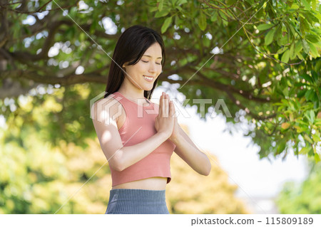 Woman doing yoga in green park (outdoor portrait, hands together in prayer, concentration, relaxation) 115809189