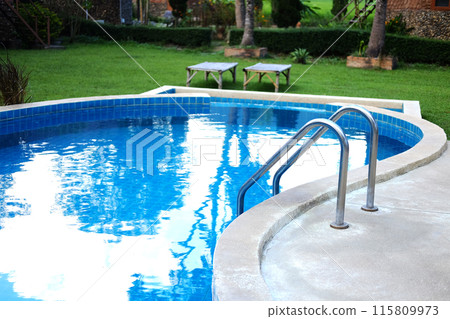 Stainless steel handrail in blue water and ceramic tiles in swimming pool outdoor in garden of resort and hotel 115809973