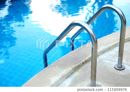 Stainless steel handrail in blue water and ceramic tiles in swimming pool outdoor in garden of resort and hotel 115809976
