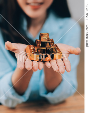 Portrait of a beautiful young businesswoman holding gold bar at office desk 115810589