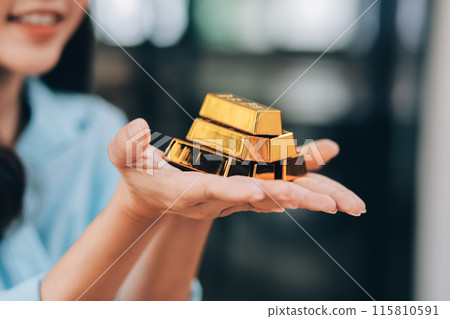Portrait of a beautiful young businesswoman holding gold bar at office desk 115810591