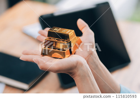 Portrait of a beautiful young businesswoman holding gold bar at office desk 115810593