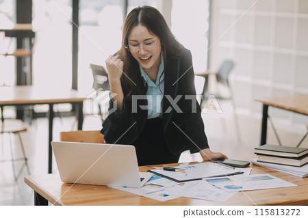 Happy young asian businesswoman sitting on her workplace in the office. Young woman working at laptop in the office. 115813272