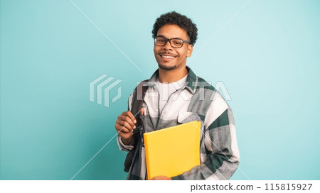Happy male university student with backpack and books in blue studio Happy male university student with backpack and books in blue studio 115815927
