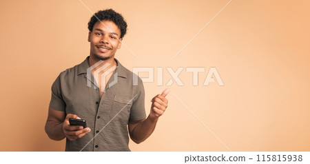 Happy man using cellphone and pointing sideways in beige studio Happy man using cellphone and pointing sideways in beige studio 115815938