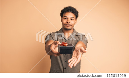 Happy man giving gift box and looking at camera in beige studio 115815939
