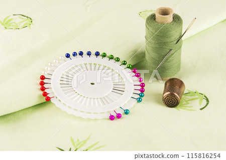 Dressmaker pins with a spool of thread and a thimble on the material Dressmaker pins with a spool of thread and a thimble on the material 115816254