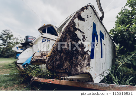 Old and rusty motor boats on a landfill surrounded by tropical forest 115816921
