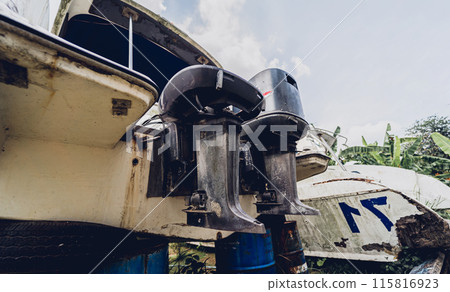 Old and rusty motor boats on a landfill surrounded by tropical forest 115816923