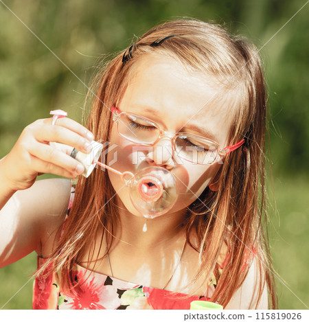 Little girl having fun blowing soap bubbles in park. Little girl having fun blowing soap bubbles in park. 115819026