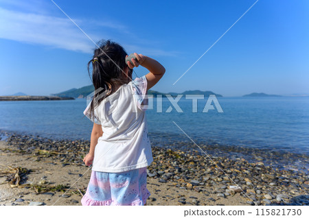 Girl throwing pebbles into the sea on the beach, back view 115821730