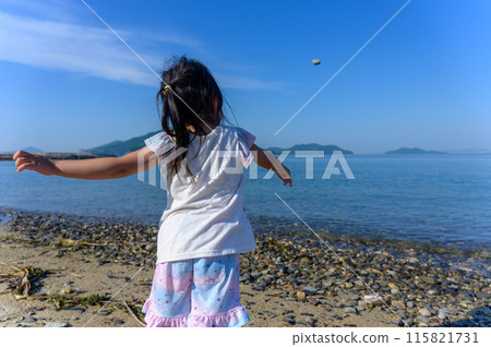 女孩在海岸上向大海丟鵝卵石，後視 115821731