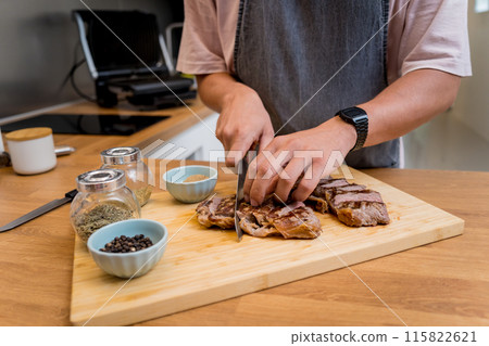 Chef at the kitchen preparing beef steaks on the home electric grill Chef at the kitchen preparing beef steaks on the home electric grill 115822621