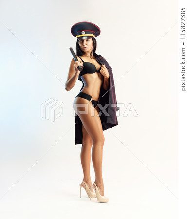 Sexy girl in a police military uniform posing in her underwear with a police rubber baton on a white background 115827385