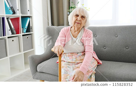 Elderly Woman Sitting On A Living Room Sofa With Cane Laughing And Looking Into The Camera 115828352