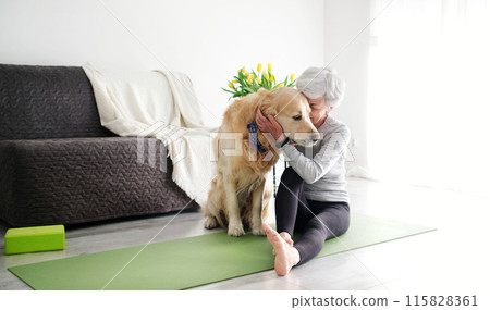 Elderly Woman With A Smile, Actively Hugging Her Dog On A Yoga Mat At Home Elderly Woman With A Smile, Actively Hugging Her Dog On A Yoga Mat At Home 115828361