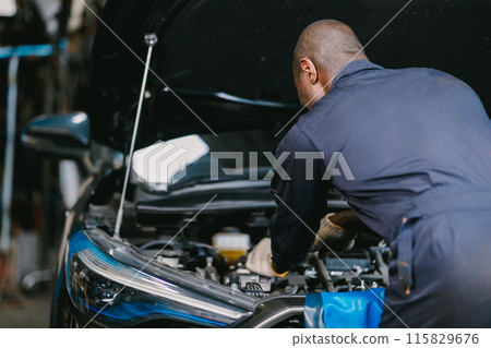 Garage Mechanic African Black male professional working car auto service checking engine oil at front hood. Garage Mechanic African Black male professional working car auto service checking engine oil at front hood. 115829676