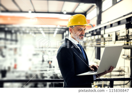 Portrait of project manager standing in modern industrial factory, holding notebook. Manufacturing facility with robotics, robotic arms and automation. Storing products and materials in warehouse. Portrait of project manager standing in modern industrial factory, holding notebook. Manufacturing facility with robotics, robotic arms and automation. Storing products and materials in warehouse. 115830847