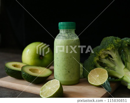 Nutritious green smoothie in bottle surrounded by avocado, lime, broccoli, apple, cucumber. Ideal for smoothie lovers and wellness content. Emphasize health benefits and freshness of this smoothie. 115830851