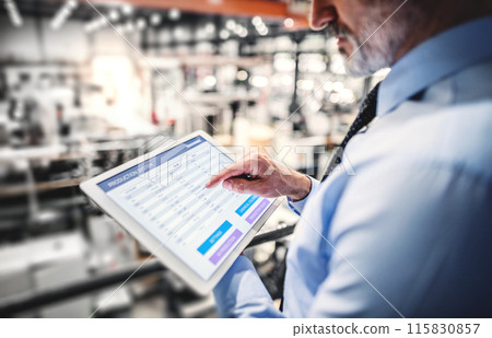 Portrait of project manager standing in modern industrial factory, holding tablet. Manufacturing facility with robotics, robotic arms and automation. Storing products and materials in warehouse. Portrait of project manager standing in modern industrial factory, holding tablet. Manufacturing facility with robotics, robotic arms and automation. Storing products and materials in warehouse. 115830857