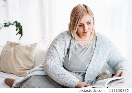 Portrait of beautiful young overweight woman at home, reading book in living room, enjoying peaceful weekend day. 115830885