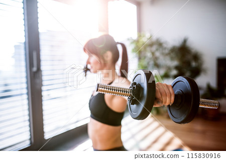 Beautiful redhead woman's home workout routine with dumbbell. Home fitness workout in living room, sporty woman wearing sportswear. 115830916