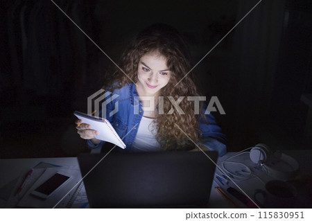 A beautiful university student having evening online class, e-learning sitting at home. Online consultation. A beautiful university student having evening online class, e-learning sitting at home. Online consultation. 115830951