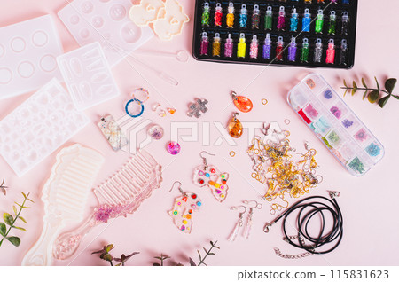 Epoxy resin jewelry and comb, molds and glitter on pink background top view 115831623