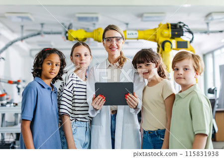 Portrait of children learning robotics in Elementary school, standing with female teacher. After-school robotics club, or field trip to real robotics laboratory. Portrait of children learning robotics in Elementary school, standing with female teacher. After-school robotics club, or field trip to real robotics laboratory. 115831938