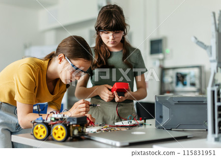 Two girl classmates working togeter on circuit board, building robotic car in after-school robotics club. Children learning robotics in Elementary school. 115831951