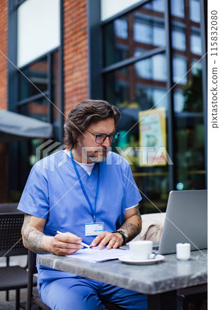 Doctor enjoying cup of coffee in coffee shop, working on laptop. Telemedicine consultation online. Mental health and life balance for a healthcare worker. Doctor enjoying cup of coffee in coffee shop, working on laptop. Telemedicine consultation online. Mental health and life balance for a healthcare worker. 115832080
