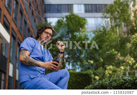 Healthcare worker taking a break, smoking a cigarette outdoors and drinking coffee from travel mug, in front of the hospital building. 115832087