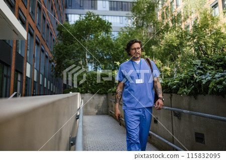 Doctor in uniform going home from work, walking in front of hospital building. Work-life balance of healthcare worker. 115832095
