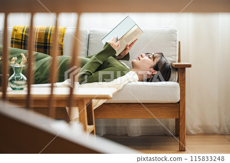 一個女人在家裡的沙發上看書 115833248