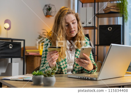Smiling woman using bank credit card and smartphone for online shopping payments at home office 115834408