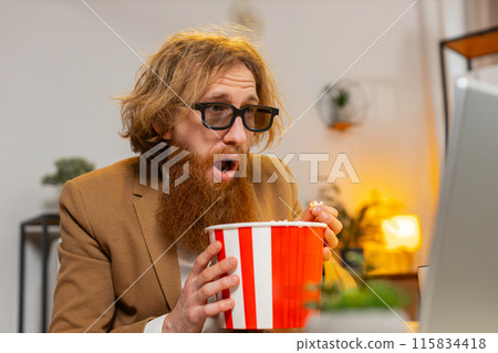 Business man taking break from work wearing 3D glasses earing popcorn watching movie on laptop 115834418