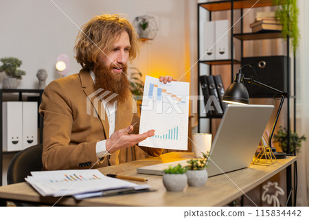 Businessman working on laptop at home office desk talks on online communication webcam video call Businessman working on laptop at home office desk talks on online communication webcam video call 115834442