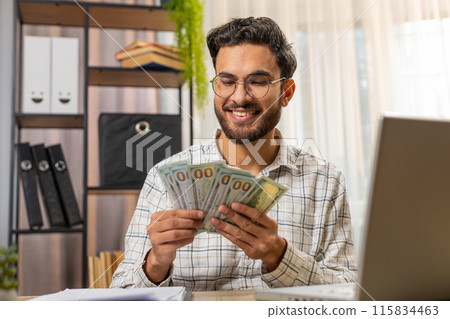 Indian business man counting money cash calculates dividends and using laptop in home office 115834463