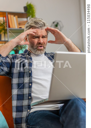 Upset senior man using laptop having anxiety stress reacting to loss bad news sitting on home sofa Upset senior man using laptop having anxiety stress reacting to loss bad news sitting on home sofa 115834498