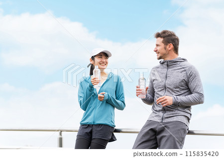 Man and woman in sportswear resting and hydrating during training in the park Man and woman in sportswear resting and hydrating during training in the park 115835420
